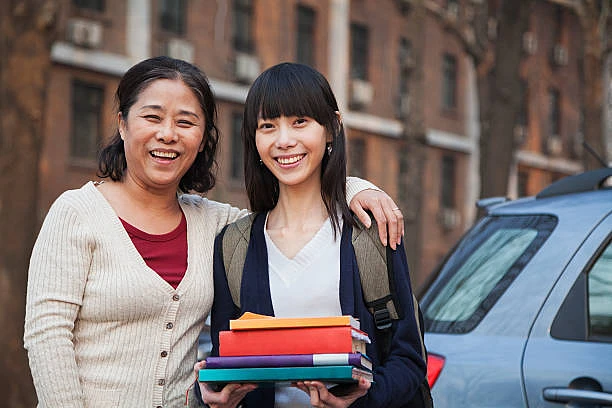 Mother and daughter portrait in front of dormitory, daughter holds a stack of books