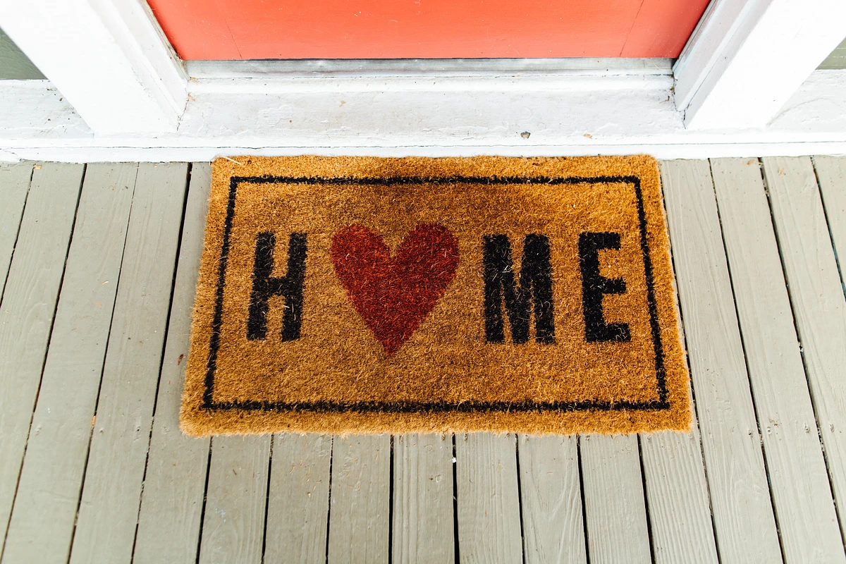 Doormat on a porch that says "HOME" with a heart shape in place of the O