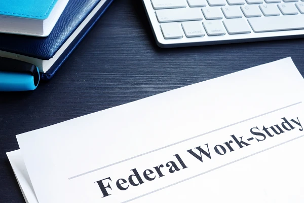 A document labeled "Federal Work-Study" is on a desk near a keyboard and notebooks.