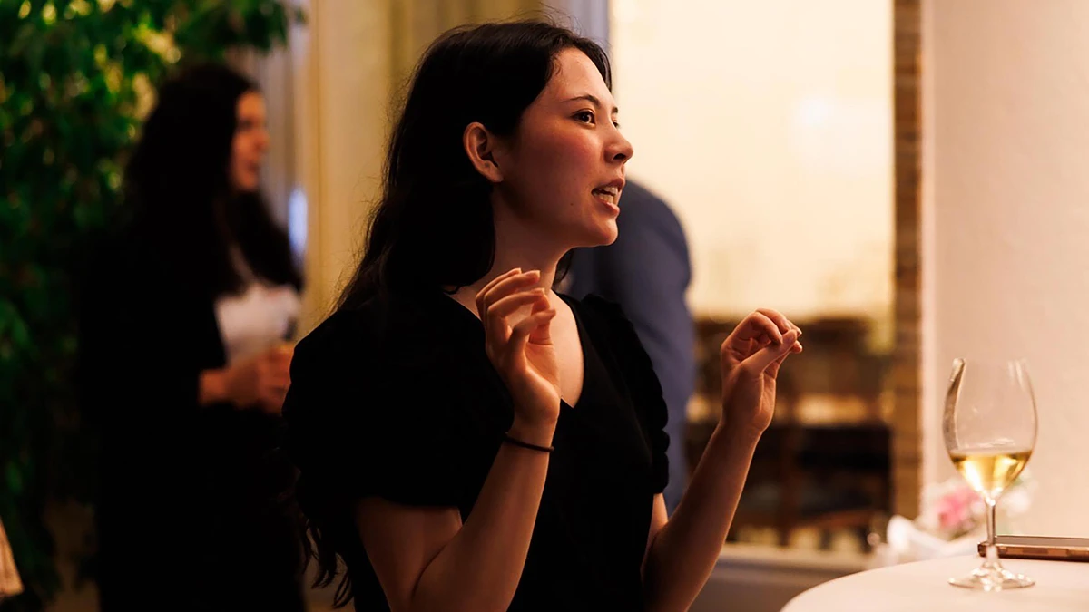 A person is engaging in conversation at a social gathering with a glass of wine on the table.